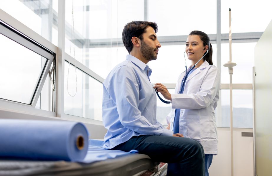 Latin American female doctor examining a patient at her office and listening to his heart with a stethoscope