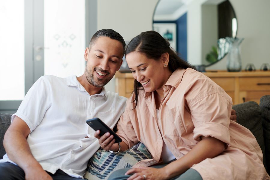a young couple looks at a cell phone together while sitting on a couch in a home