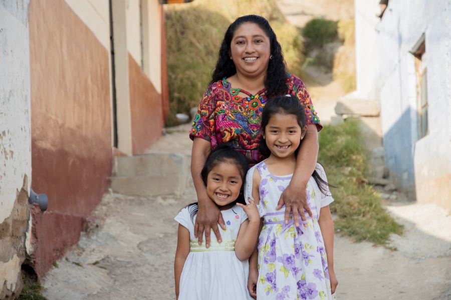 Hispanic mother hugging her daughters outside her house in rural area